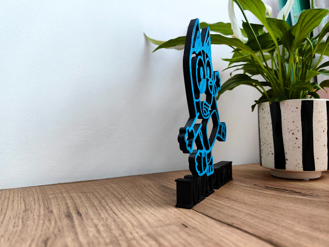 Персонализирана 3D стойка Bluey & Bingo на дървена маса с растение на заден план.